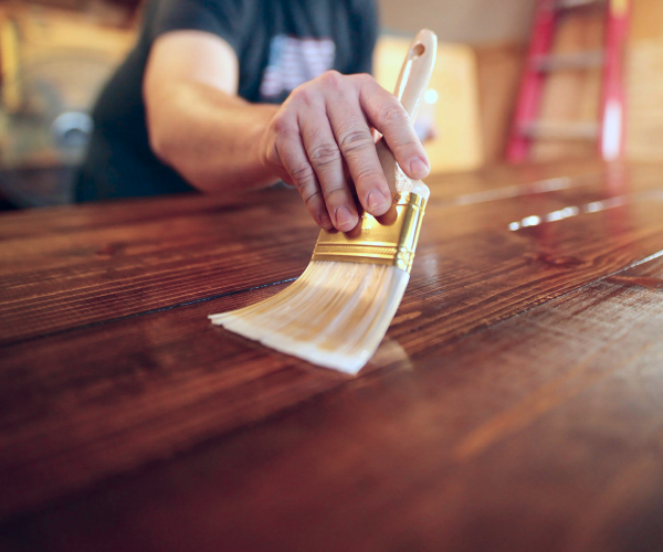 person with paintbrush varnishing flooring materials